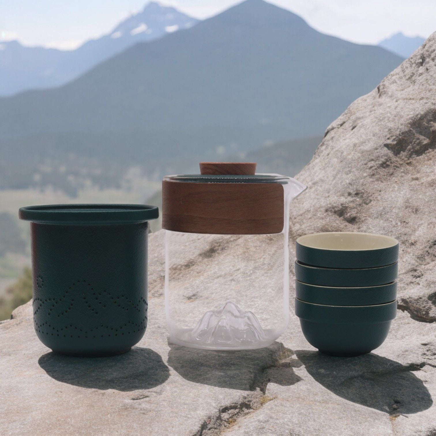 Glass travel teapot with a mountain design inside, featuring a removable infuser and four matching small glass cups.
