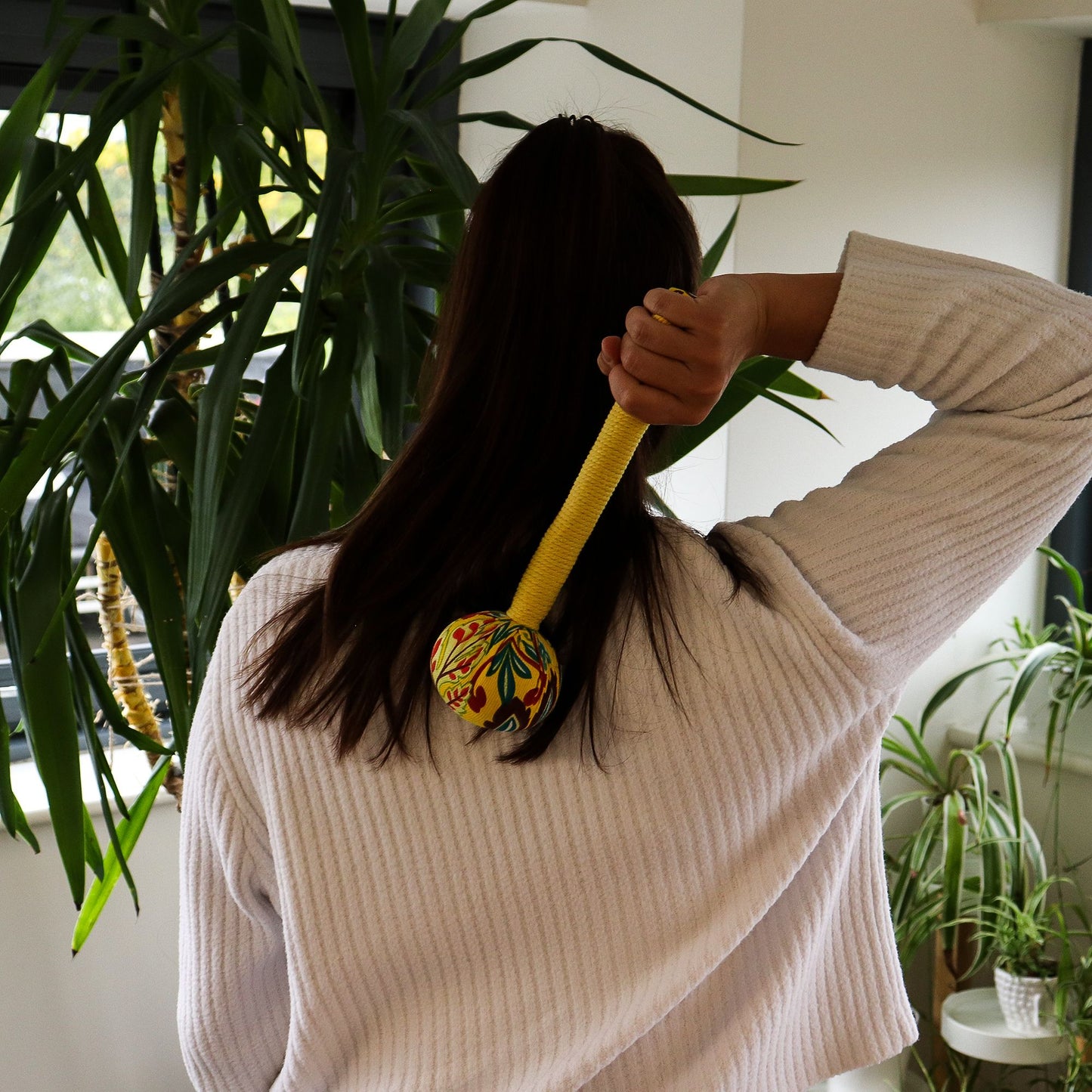 Yellow fabric massage hammer with a bamboo handle and herbal wormwood filling for muscle relaxation.
