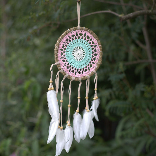 Intricate pastel pink macramé dream catcher with a woven web and hanging soft pink threads and beads.
