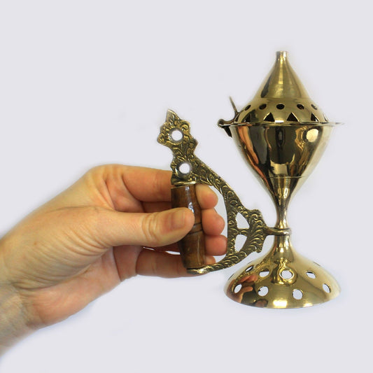 Polished brass incense cone burner with a decorative vented lid, sturdy base, and a smooth dark wooden handle.