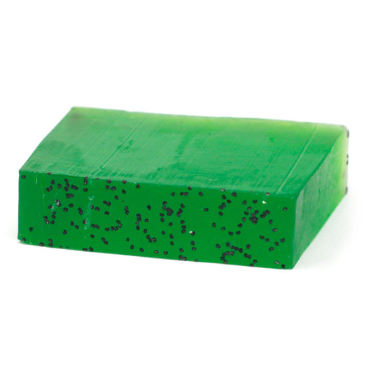 A rustic slice of green hand-crafted soap with a textured top, showing natural botanical inclusions.