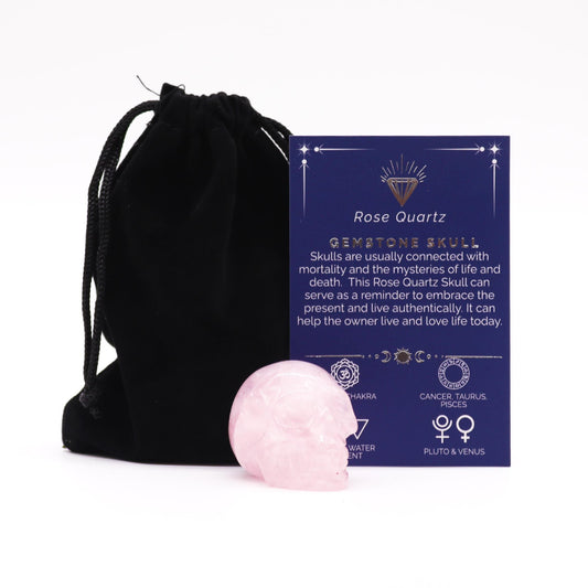 A small, polished pink rose quartz gemstone carved into the shape of a realistic human skull.