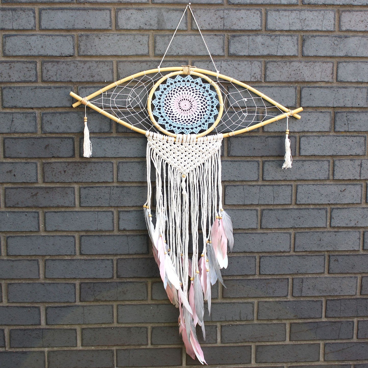 Large blue, white, and pink macrame dream catcher featuring a central woven evil eye design and hanging tassels.