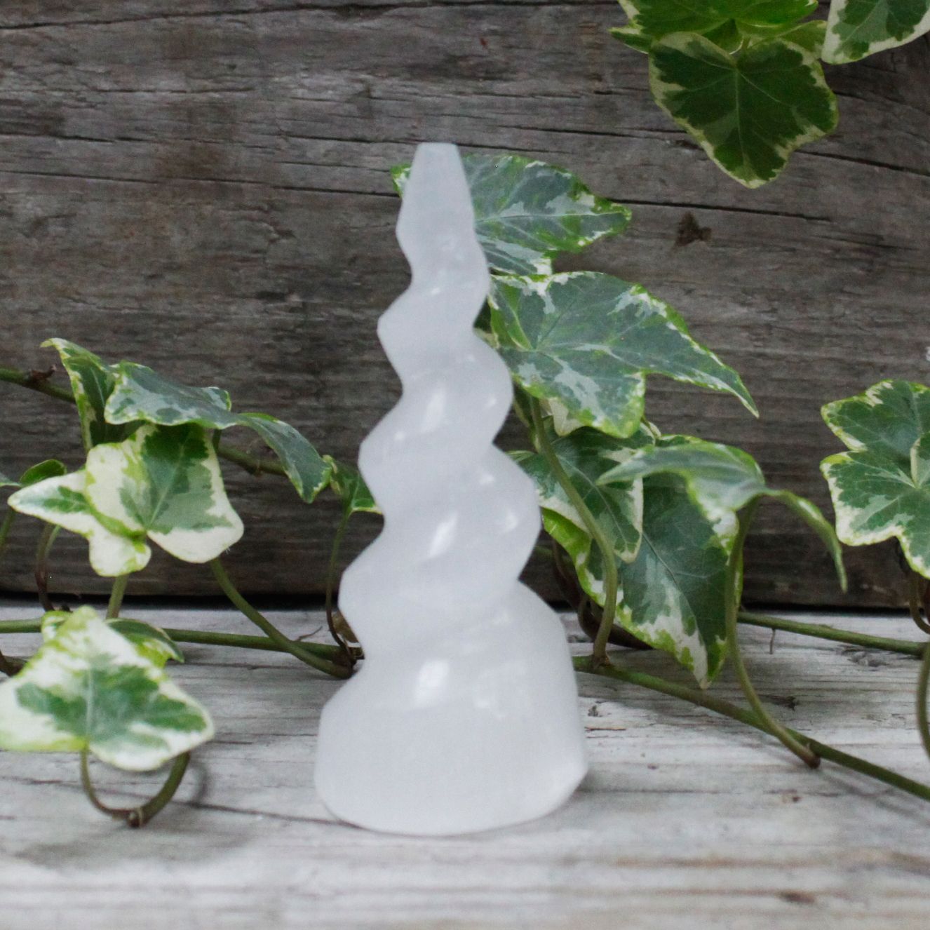 White selenite crystal tower carved into a spiral unicorn horn shape with a luminous pearly finish.