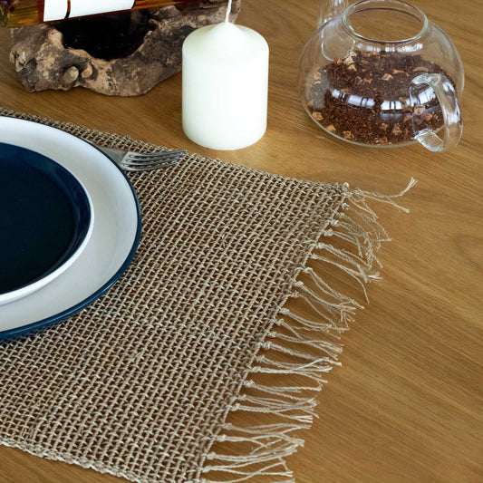 Round natural woven seagrass placemat with a decorative fringed edge on a neutral background.