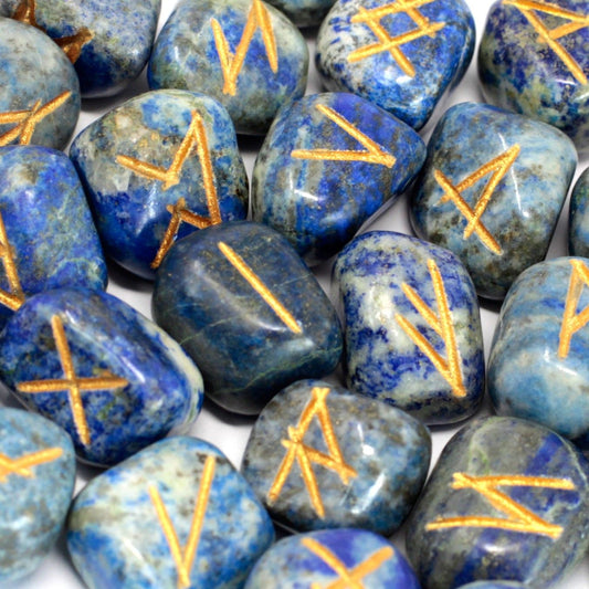 Deep blue Lapis Lazuli rune stones with gold engraved symbols spread beside a small velvet drawstring pouch.