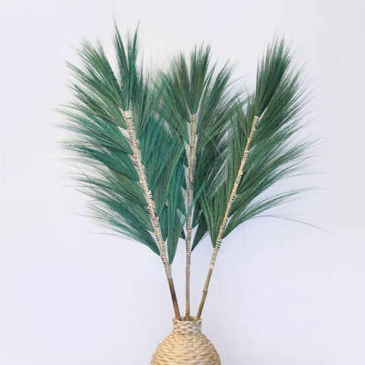 Tall green rayung grass stems braided onto bamboo sticks, standing in a minimalist interior setting.