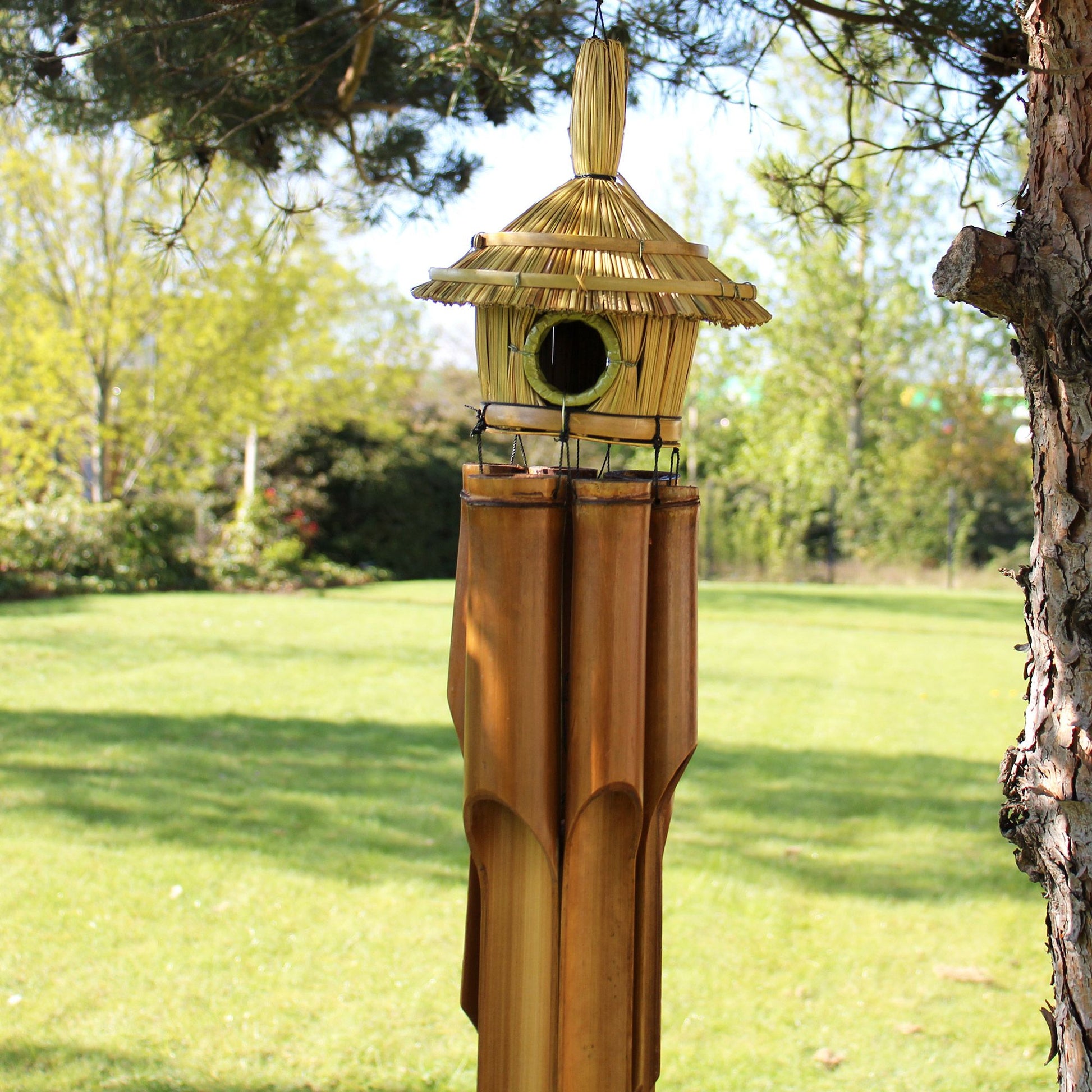 Large round woven seagrass bird house with integrated wooden chimes hanging from the base.