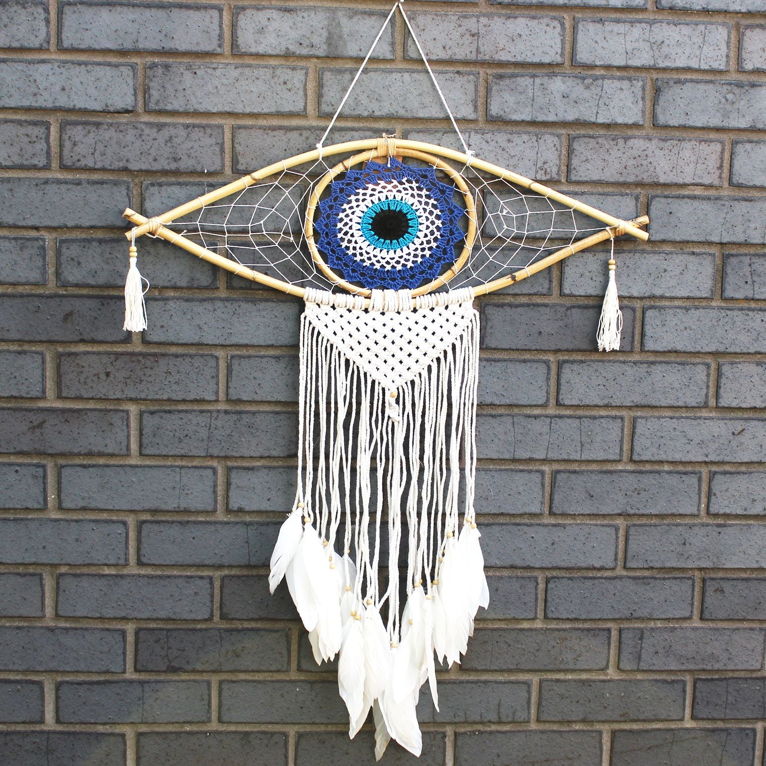 Large macrame dream catcher featuring a blue and white evil eye design with flowing black and white cotton tassels.