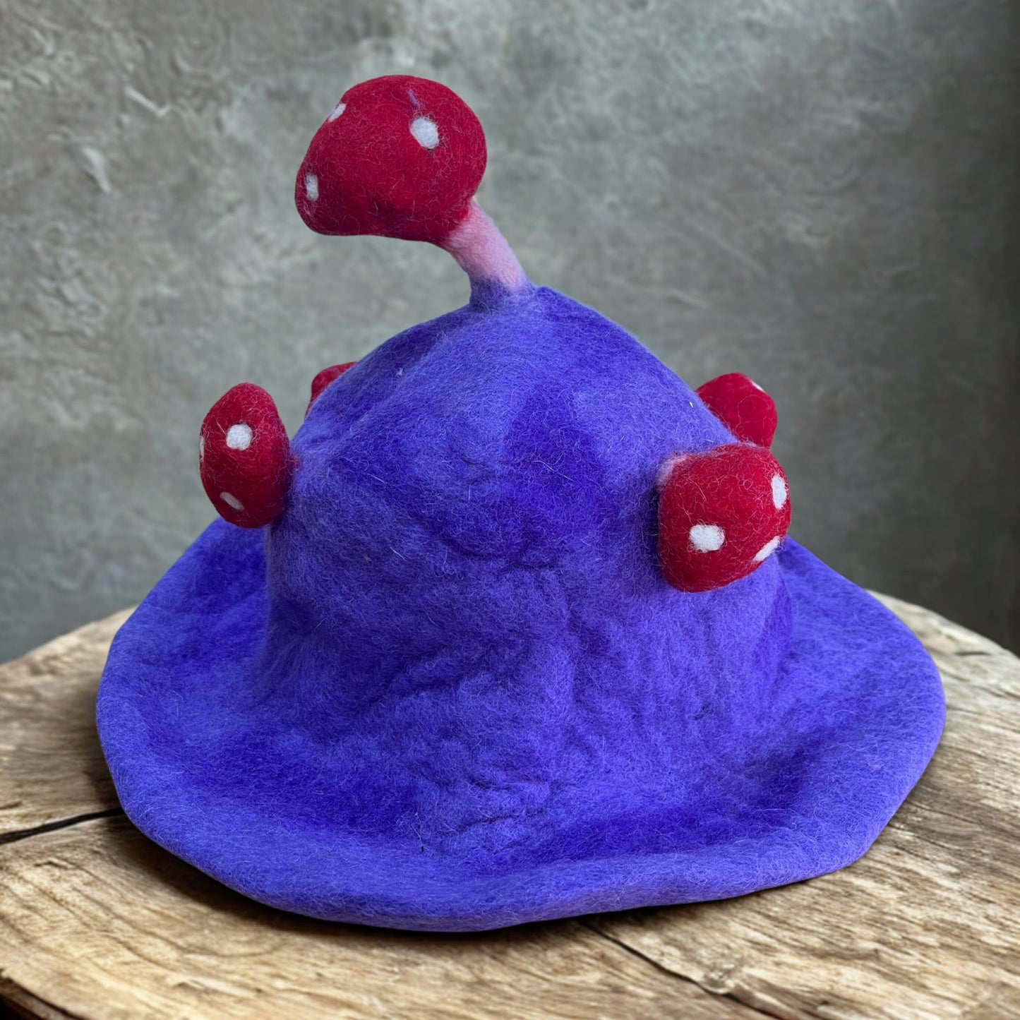 Handcrafted felted mushroom hat in shades of dreamy purple and lavender with white spots and a whimsical pointed top.
