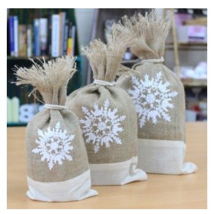 Three sturdy white jute pouches featuring a classic Christmas snowflake design, ideal for holiday gift giving.