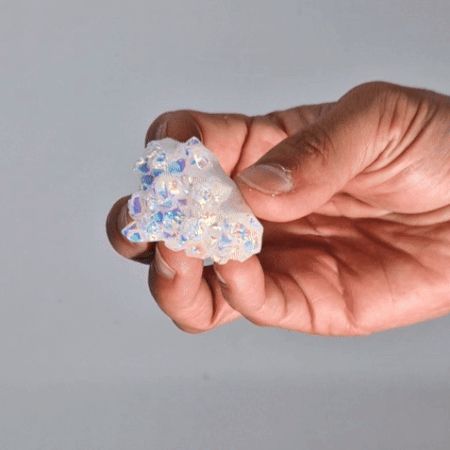A small, shimmering iridescent Angel Aura Quartz crystal with a rainbow-like metallic sheen and natural jagged edges.