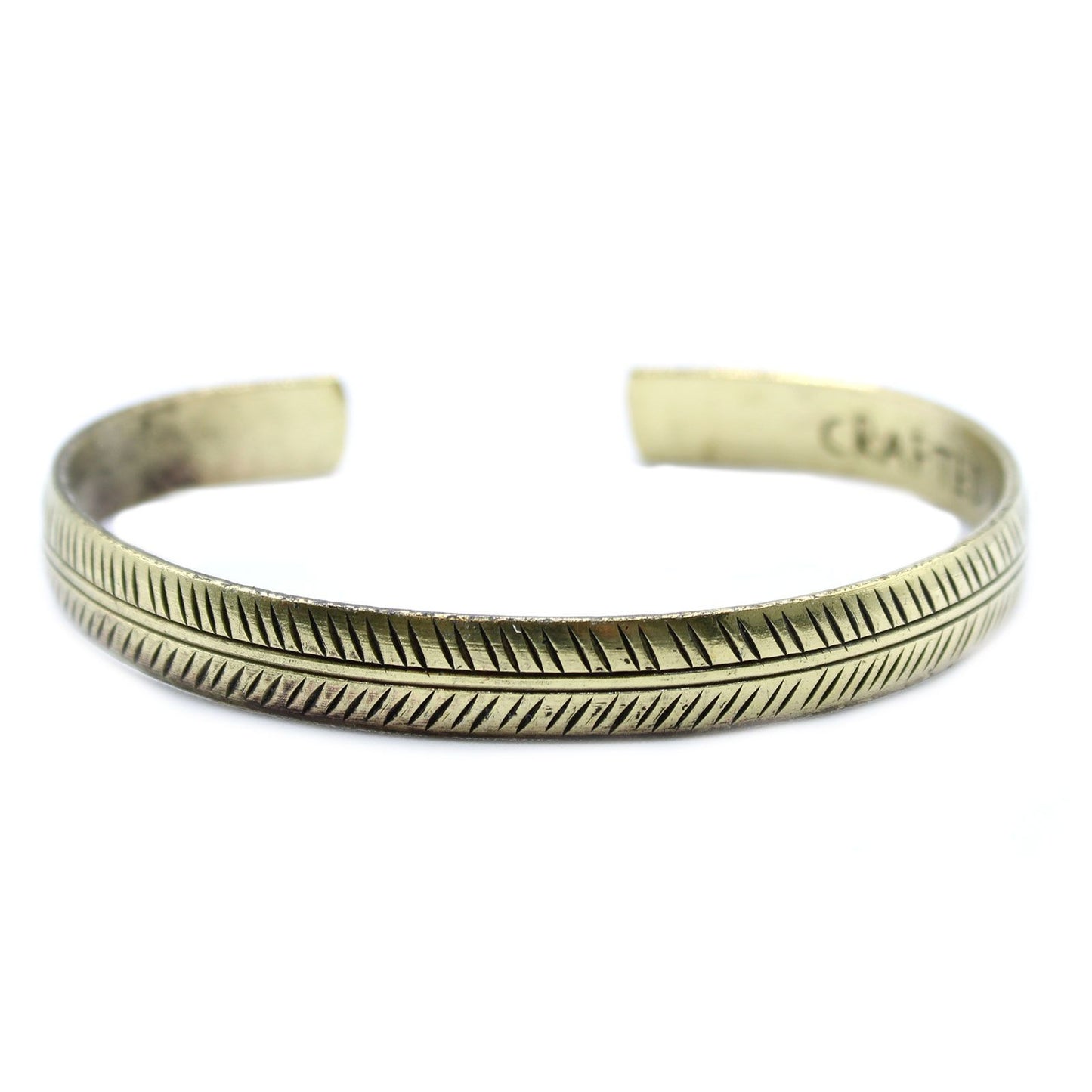 Close-up of a slim brass cuff bracelet featuring an intricate etched tribal leaf pattern with a vintage finish.