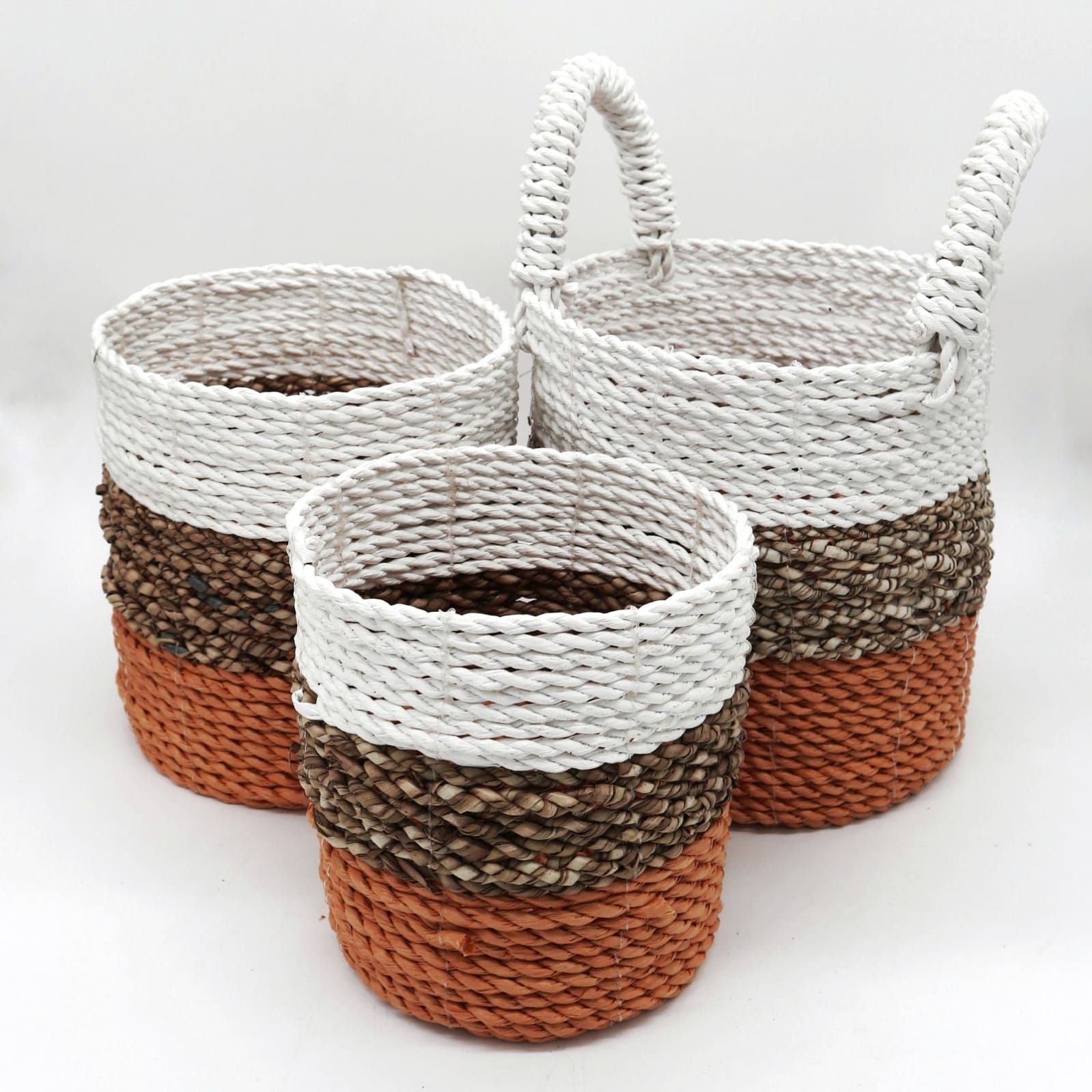 Set of three handwoven round seagrass baskets featuring natural, orange, and white horizontal stripes.