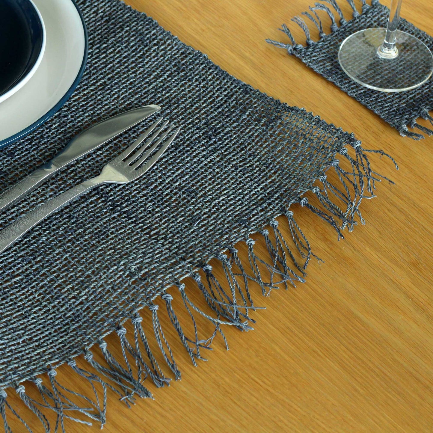 Handwoven charcoal grey seagrass placemat featuring a natural texture and decorative fringe border on a plain surface.