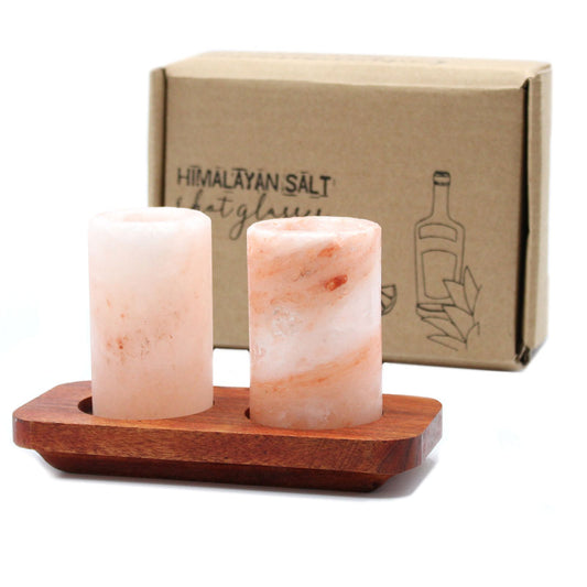 Two pink Himalayan salt shot glasses resting on a rustic rectangular wooden serving stand.