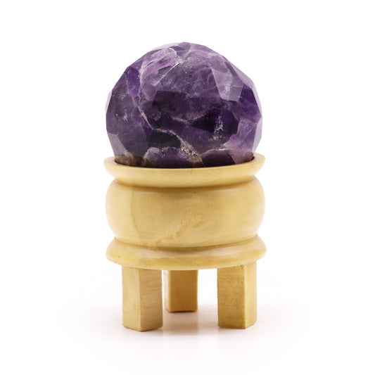 Deep purple faceted amethyst gemstone ball resting on a light brown wooden stand.