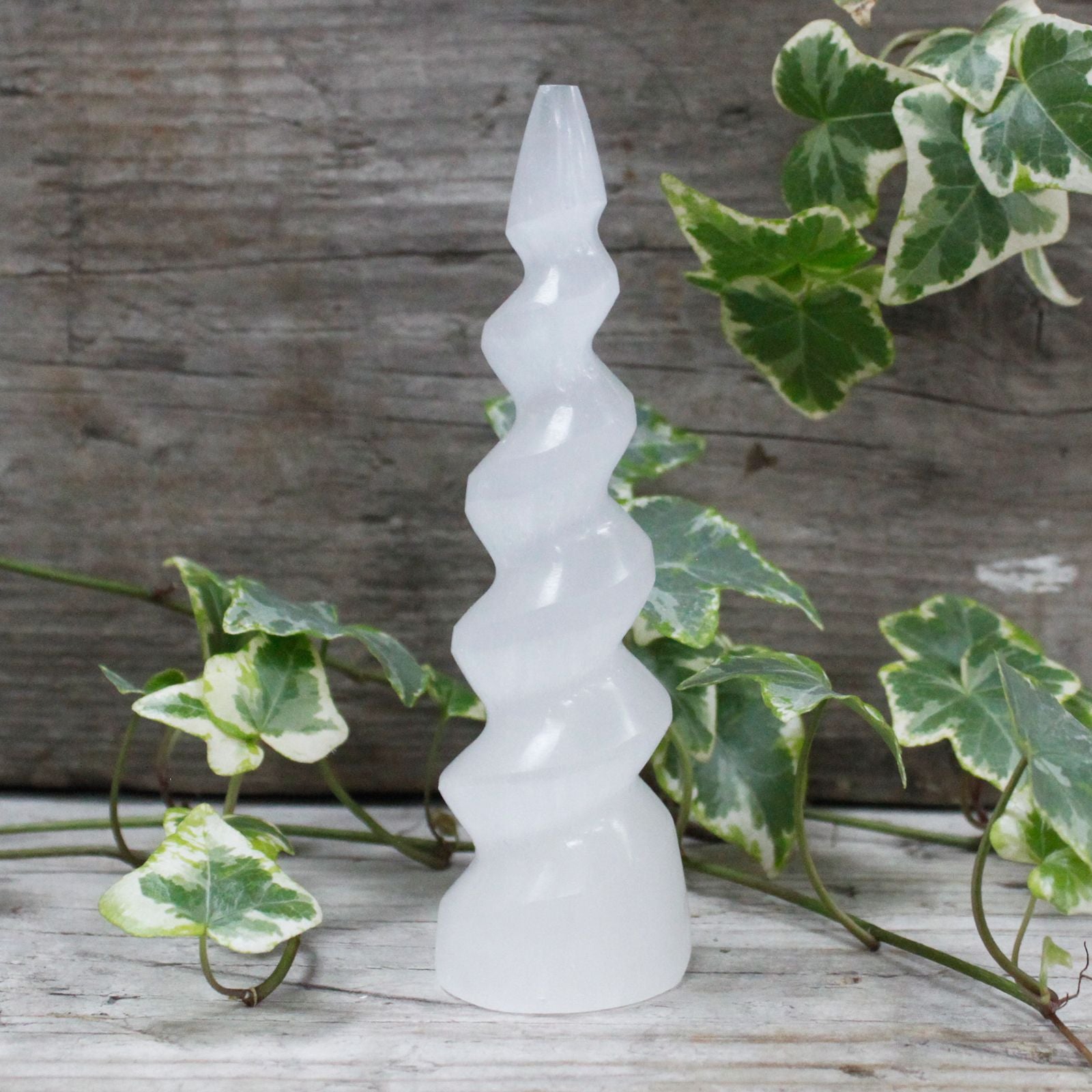 Tall white selenite crystal tower carved into a spiral unicorn horn shape with a pearly translucent finish.