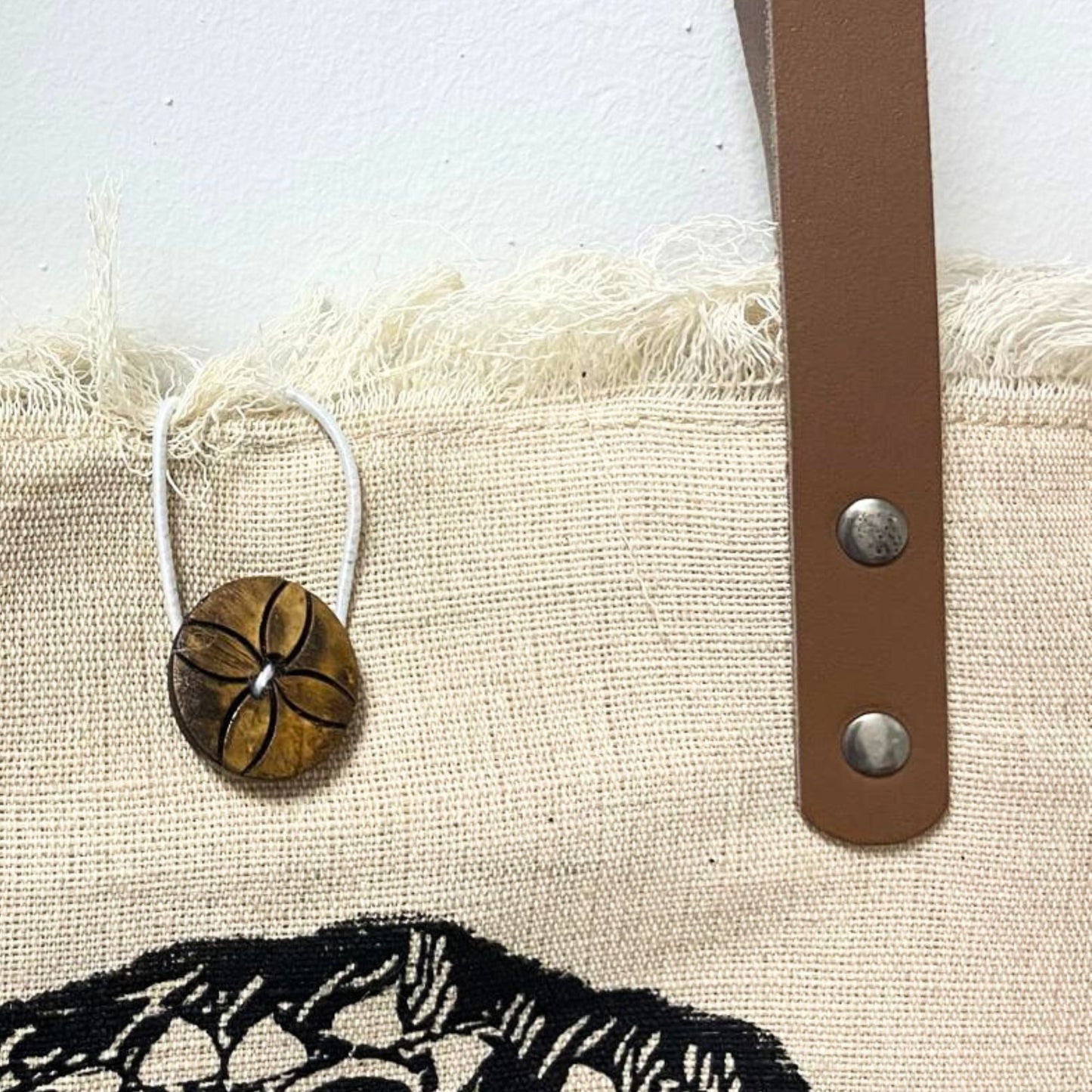 Eco-friendly natural fabric tote bag featuring sturdy brown leather handles and a unique frilly edge detail.