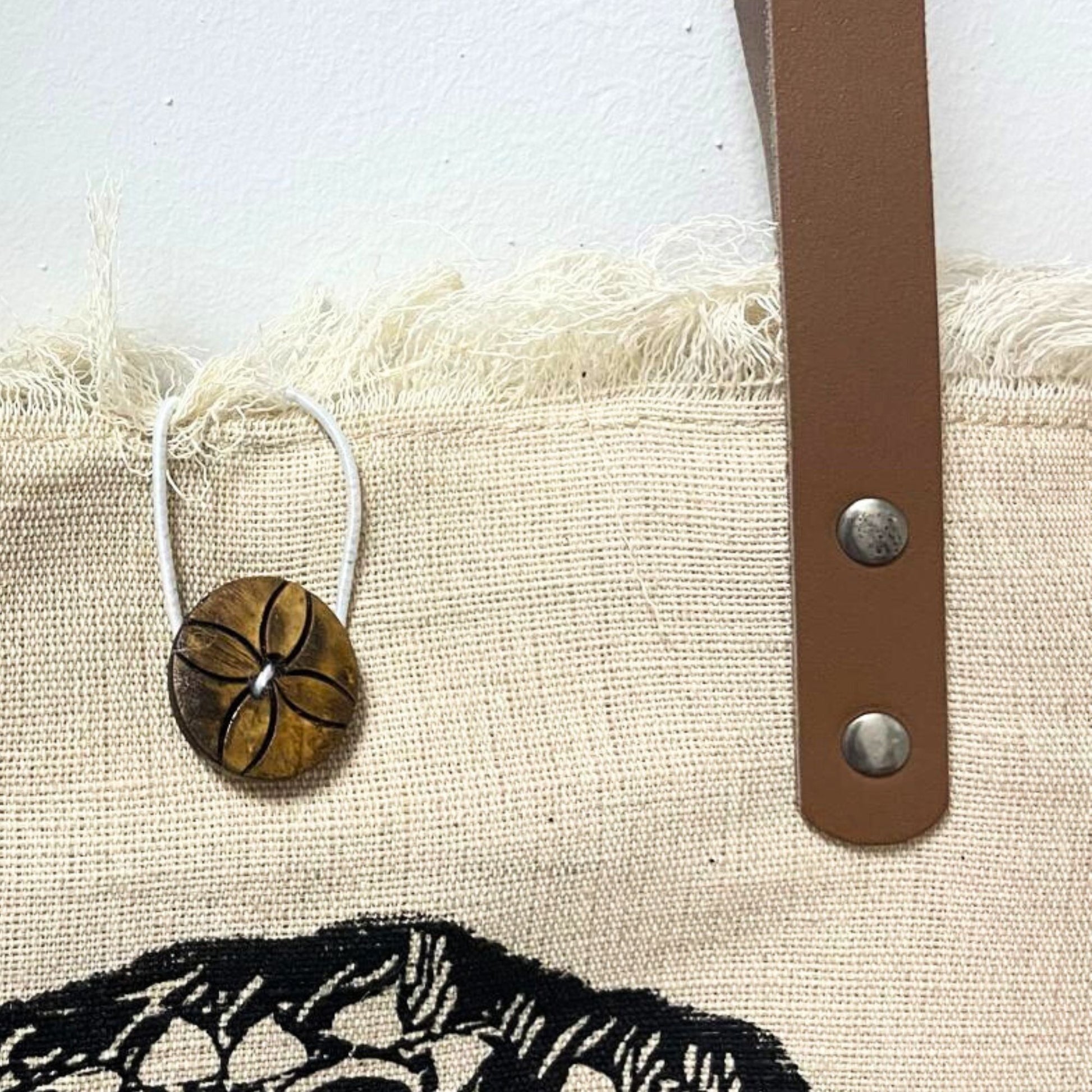 Eco-friendly natural fabric tote bag featuring sturdy brown leather handles and a unique frilly edge detail.