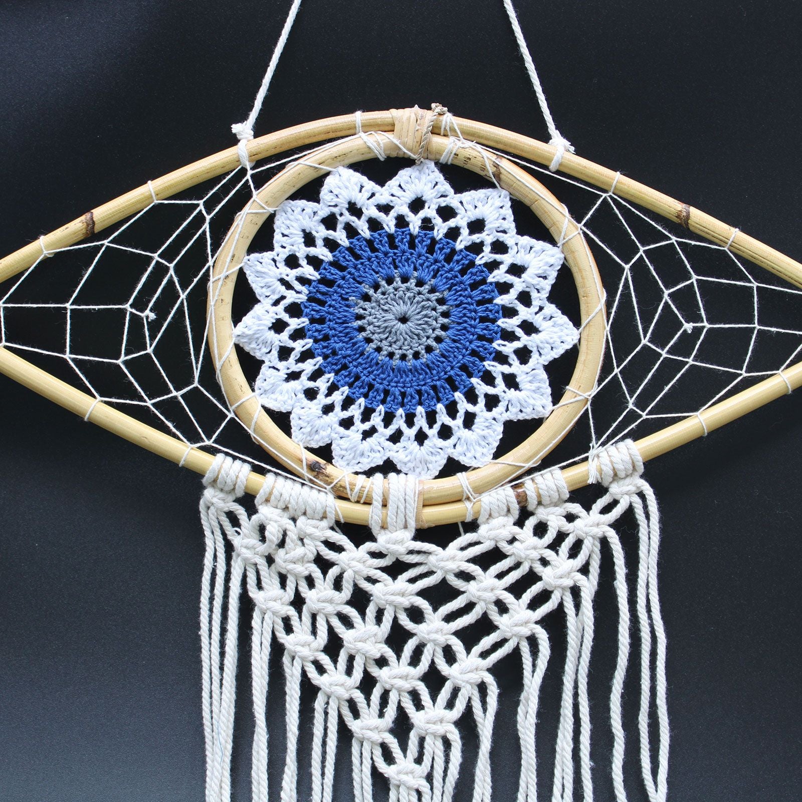 Intricate white macrame dream catcher featuring a blue and grey evil eye symbol in the centre with hanging tassels.