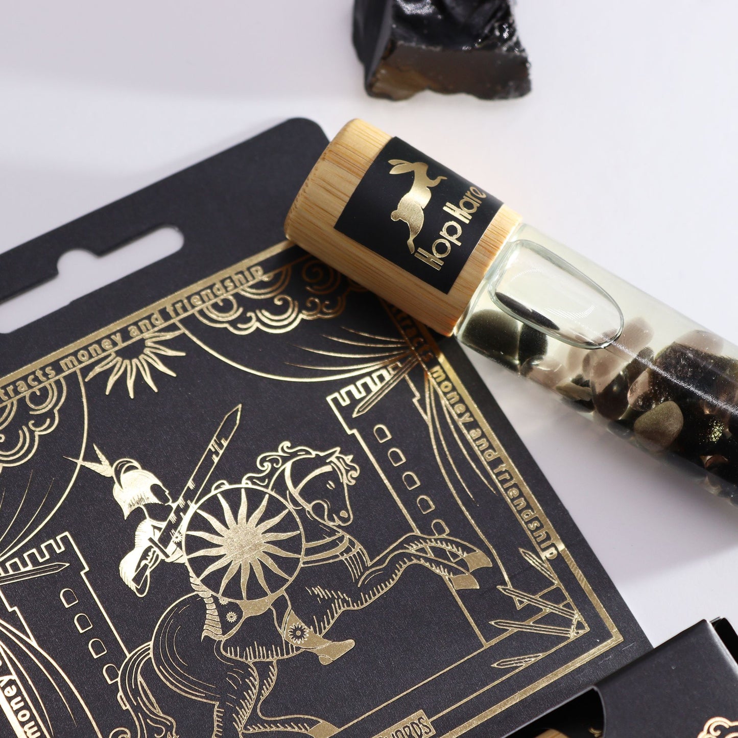 A glass essential oil gemstone roll-on bottle with black tourmaline crystals inside and a tarot-themed label.