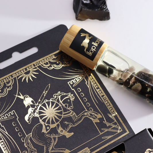 A glass essential oil gemstone roll-on bottle with black tourmaline crystals inside and a tarot-themed label.