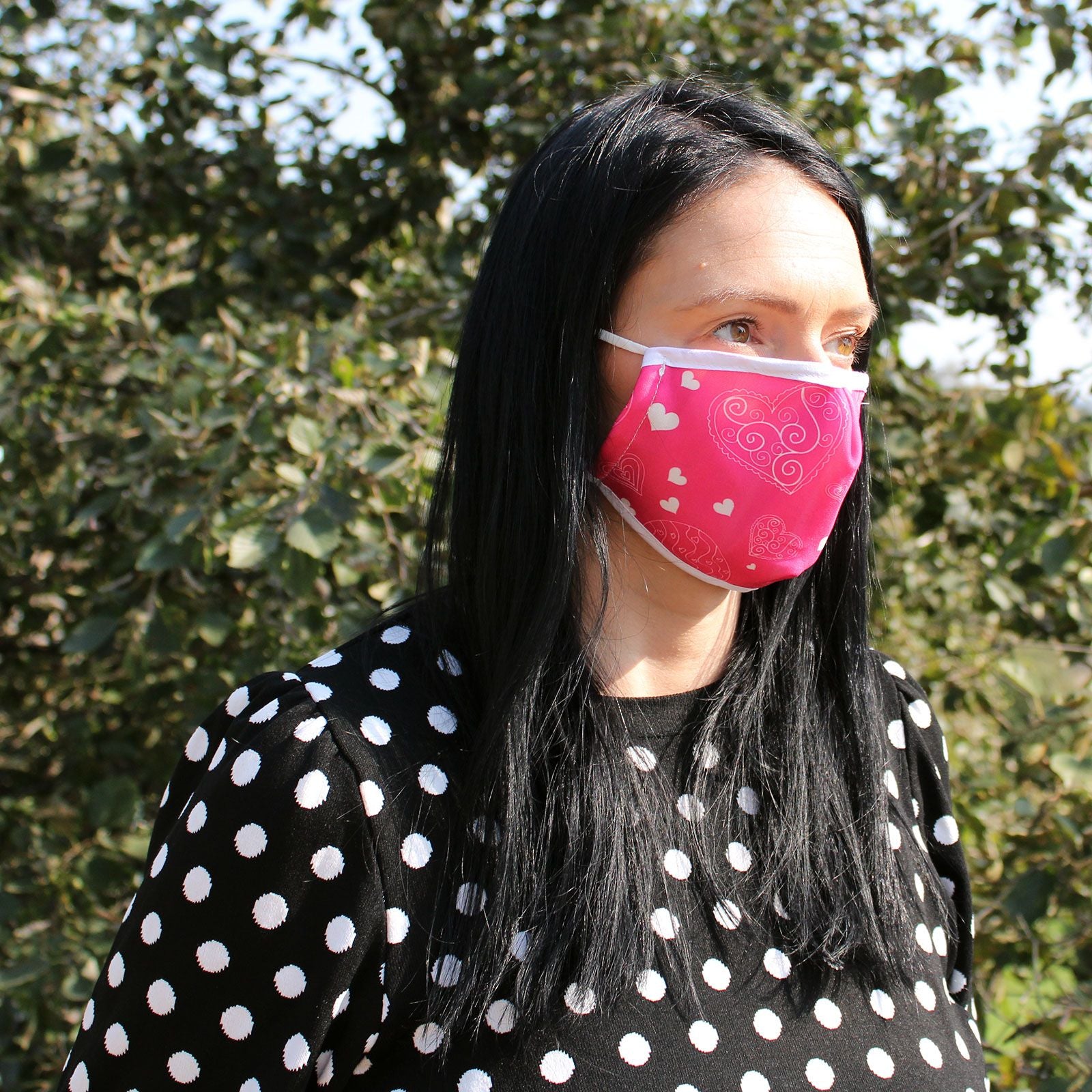 Close-up of a pink fabric face covering featuring a repeating pattern of small white and dark pink hearts.