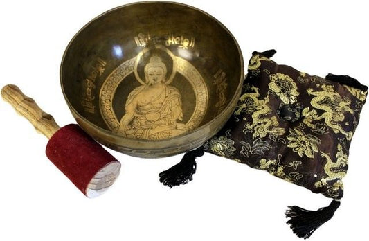 Golden brass singing bowl with Buddha engraving, resting on a decorative cushion next to a suede-coated wooden striker.